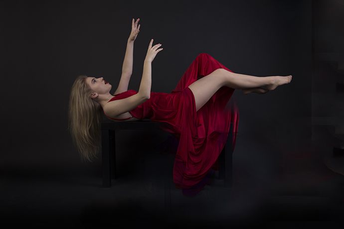 Mujer en vestido rojo cayendo con su boca abierta y con un fondo negro
