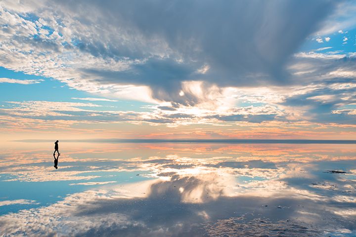 Persona anda sobre unas salinas en las que se refleja el cielo