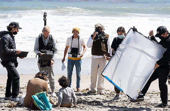 Una troupe per una produzione di video che gira la scena di una persona seduta su una spiaggia con il figlio