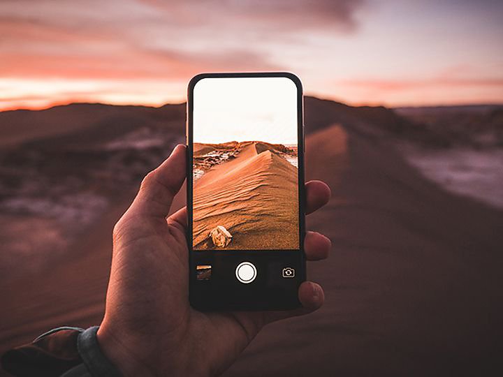 A person holding a smartphone and taking a photo of a desert environment