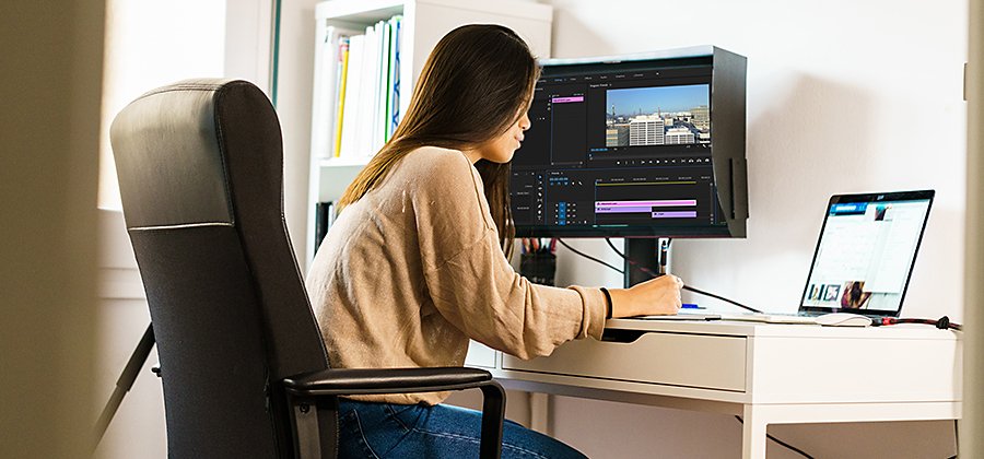 Personne assise à un bureau réalisant le montage d’une vidéo sur un ordinateur portable connecté à un second écran