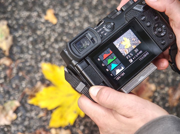 A photographer holding a DSLR camera showing the exposure settings on the camera's display screen