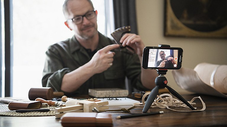 Person recording a leather-working video of themselves on their mobile phone
