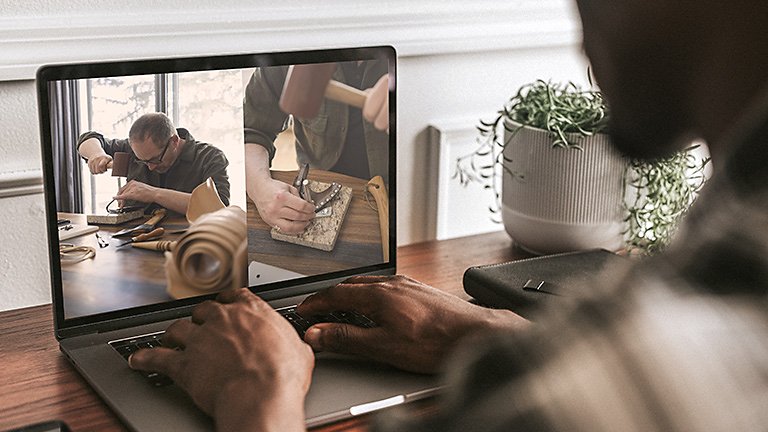 Person looking down at their laptop watching a leather-working video