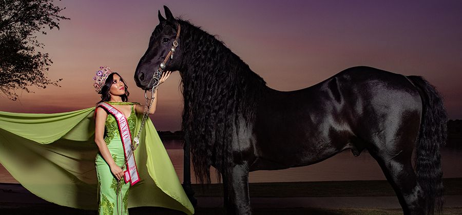 A pageant contestant for New Mexico standing in a green dress next to a tall black horse