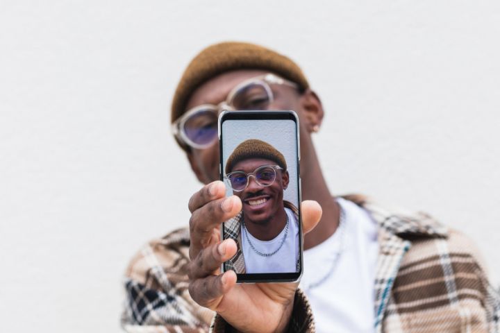 Iemand die zijn mobieltje omhoog houdt met op het scherm een selfie van hemzelf