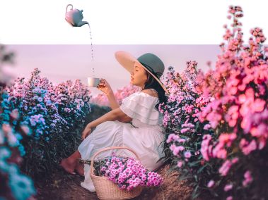 Théière en suspension dans l’air versant du thé dans une tasse tenue par une jeune fille assise dans un champ de fleurs