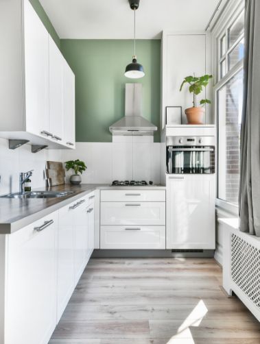 A white kitchen with green accents for a real estate listing is framed to give a sense of depth