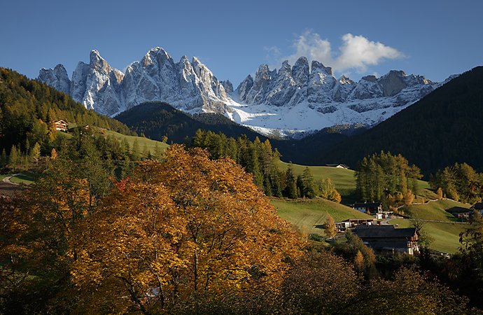 Rolling grass hills with several dwellings in front a large, snowy mountain